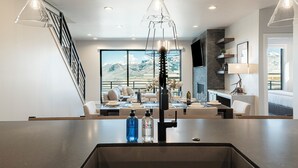 Een moderne keuken met een centraal eiland, een eethoek met uitzicht op bergen en een trap.