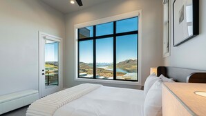 Een slaapkamer met een groot raam, een bed, een nachtkastje en een bankje.