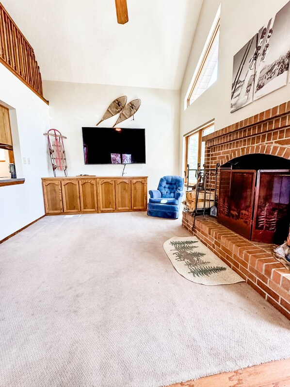 A spacious living room with a fireplace, a television mounted on the wall, and a blue armchair.
