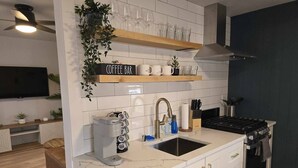 Una cocina moderna con armarios blancos, lavavajillas integrado, una barra de café con cafetera y estufa.