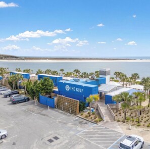 Un hôtel situé sur la côte, doté d’un parking, offrant une vue sur la plage et arborant une enseigne sur laquelle on peut lire : « THE GULF ».