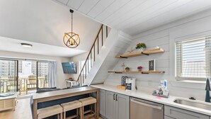 A modern kitchen with a wooden bench, a staircase, and a dining area with a view. - Skip the packed high-rises!•
Steps to Beach • Family Ready • 
Gulf View 2BR-2BA (Orange Beach)