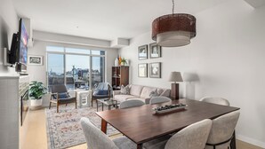 Un salon moderne comprenant une table à manger, des chaises, un canapé et une grande fenêtre donnant sur la ville.