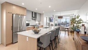 Une cuisine moderne dotée d’appareils électroménagers en acier inoxydable, d’un îlot central avec des tabourets de bar et offrant une vue sur la ville.