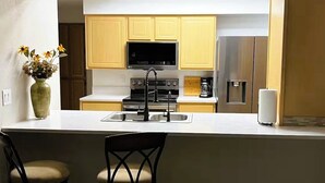 A modern kitchen with light wooden cabinets, a stainless steel refrigerator, a built-in oven, and a central island with a sink. - Style & Convenience Near PHX Ask for LongTerm Rate (Tempe)