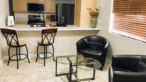 A compact kitchen with modern appliances, a dining area with a glass table and chairs, and a black leather chair. - Style & Convenience Near PHX Ask for LongTerm Rate (Tempe)