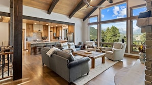 Un vaste espace de vie doté d’une grande fenêtre offrant une vue sur les montagnes, une cuisine avec des meubles en bois et un coin salon confortable agrémenté d’une cheminée.