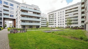 A modern apartment complex with multiple balconies, a central courtyard with grass, and bicycles parked outside.