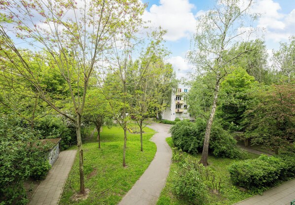 A pathway through a lush green area with trees and a building in the background.