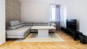 A modern living room with a sectional sofa, a white coffee table, a flat-screen TV, and a herringbone wood floor.