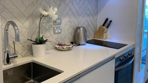 A modern kitchen with a herringbone tile backsplash, stainless steel sink, and a built-in oven. - Heart of AKL Modern Studio PoolGymSauna (Auckland)