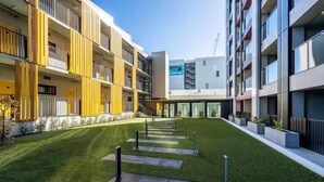 A modern apartment complex with a central courtyard, balconies, and a clear sky. - Heart of AKL Modern Studio PoolGymSauna (Auckland)