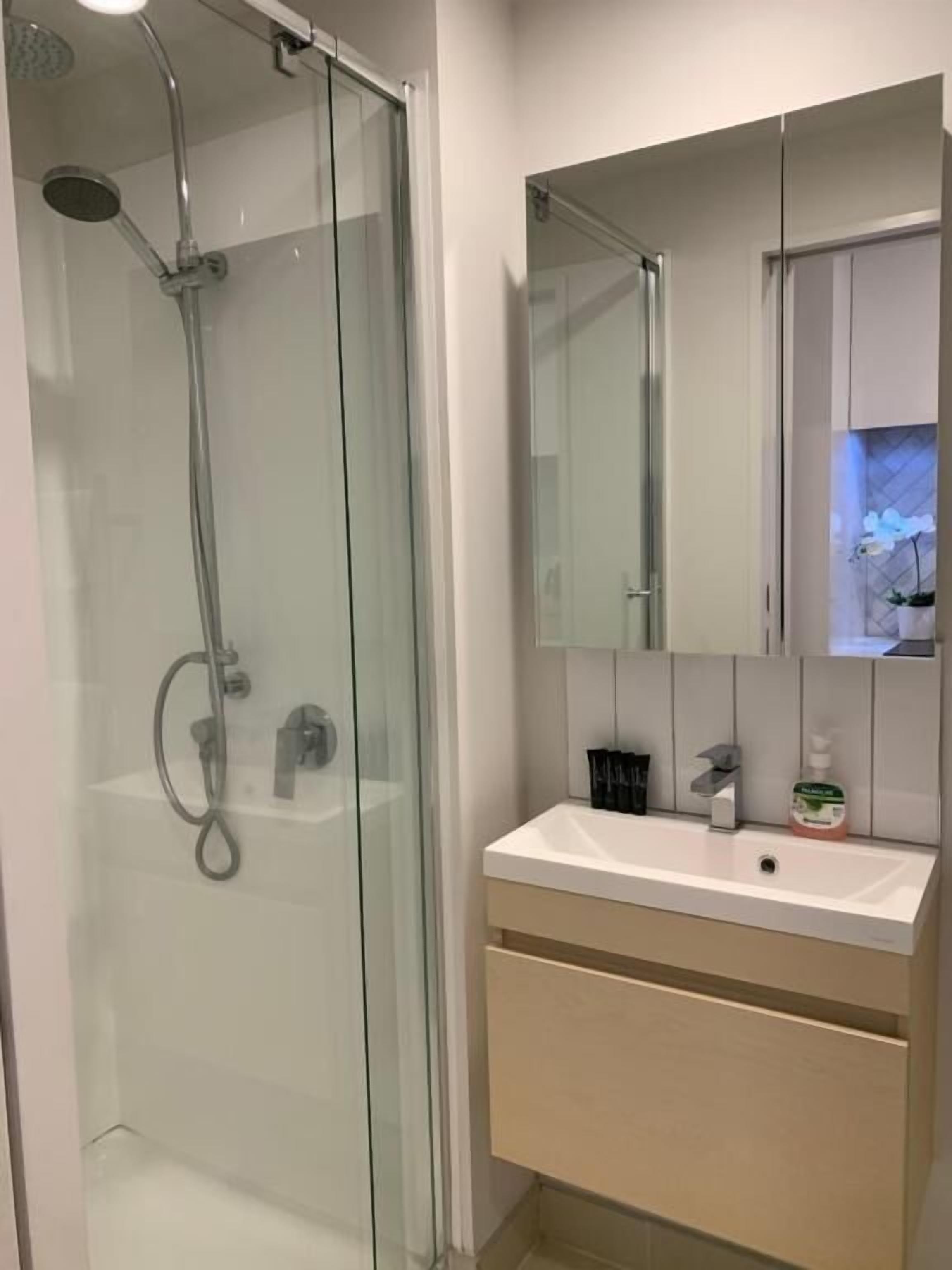 A modern bathroom with a glass-enclosed shower, a white sink, and a mirror above it.
