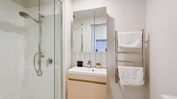 Un baño moderno con cabina de ducha de vidrio, un lavabo con espejo y un perchero con dos toallas.