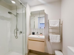 A modern bathroom with a glass shower enclosure, a sink with a mirror above it, and a towel rack with two towels.