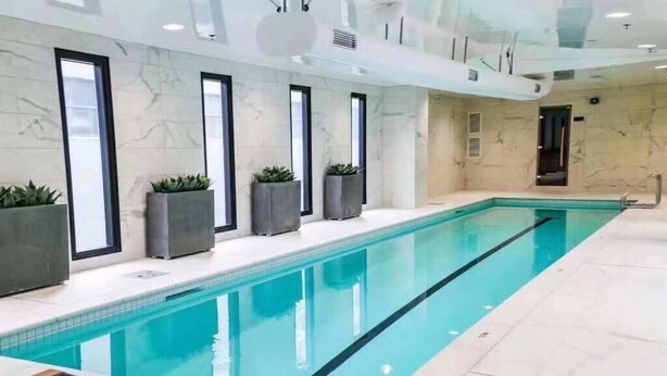 A long indoor swimming pool with clear blue water, surrounded by marble walls and large windows. - Heart of AKL Modern Studio PoolGymSauna (Auckland)