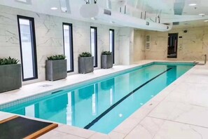 A long indoor swimming pool with clear blue water, surrounded by marble walls and large windows. - Heart of AKL Modern Studio PoolGymSauna (Auckland)