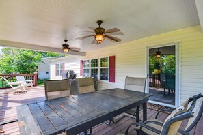 Eine Terrasse im Freien mit Holztisch und -stühlen, Deckenventilatoren und Blick auf ein Haus im Hintergrund.