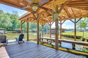Relax in a serene lakeside pavilion with a wooden deck, ceiling fan, and picturesque views of the lake.