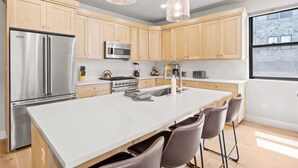 A modern kitchen with wooden cabinets, stainless steel appliances, a large island with bar stools, and pendant lighting. - Mayflower Lakeside 103 | Mountain View | Balcony | Full Kitchen | Private Bedrooms | Fireplace (Heber City)