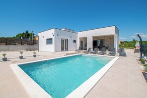 Een modern huis met twee verdiepingen, een zwembad, terras en een helder uitzicht op het omliggende landschap.