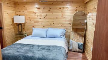 A wooden-paneled room with a bed, a bedside table with a lamp, and a mirror.