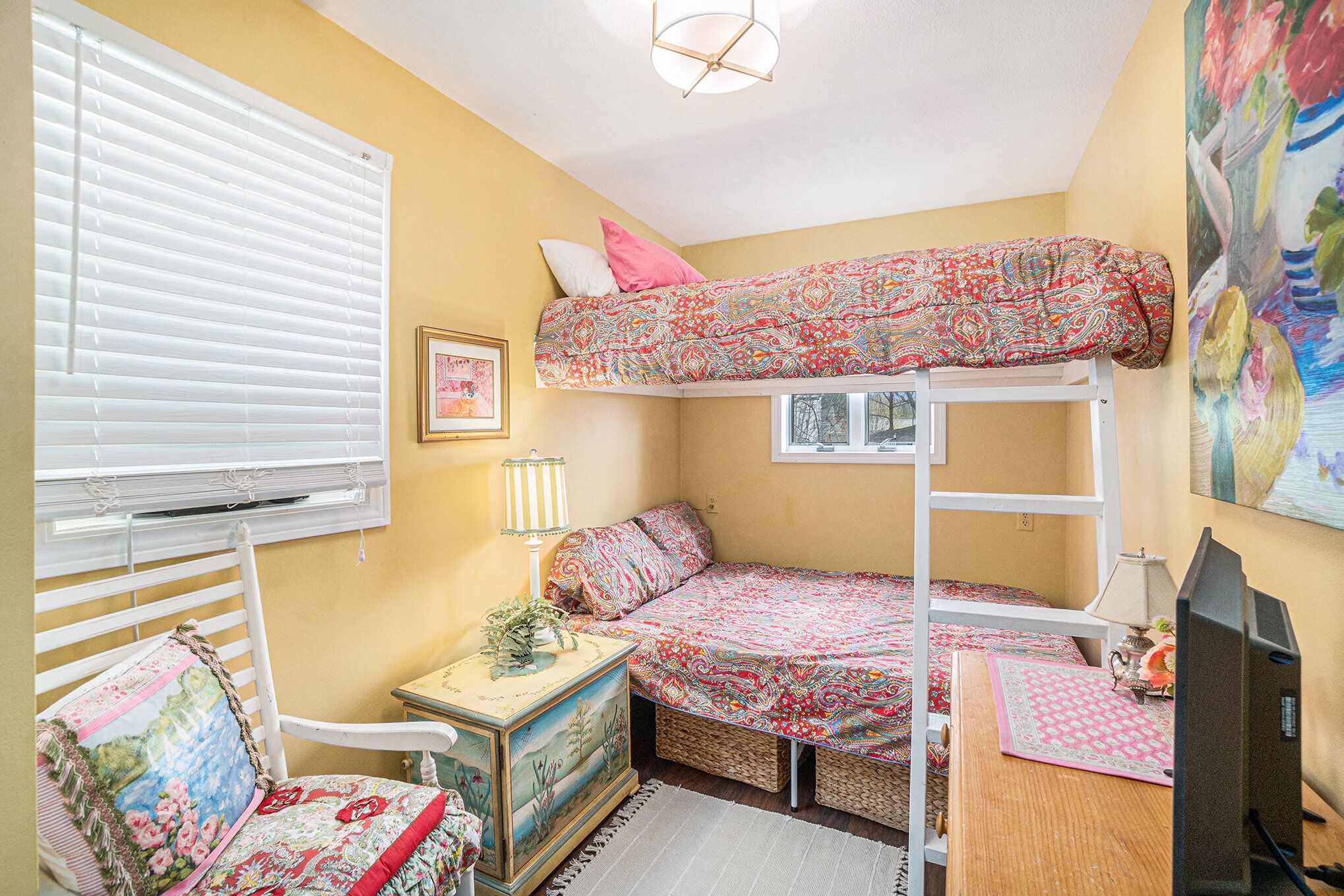 Une petite chambre à coucher, chaleureuse et accueillante, avec un lit superposé, un bureau, une chaise, une lampe et un tableau accroché au mur.