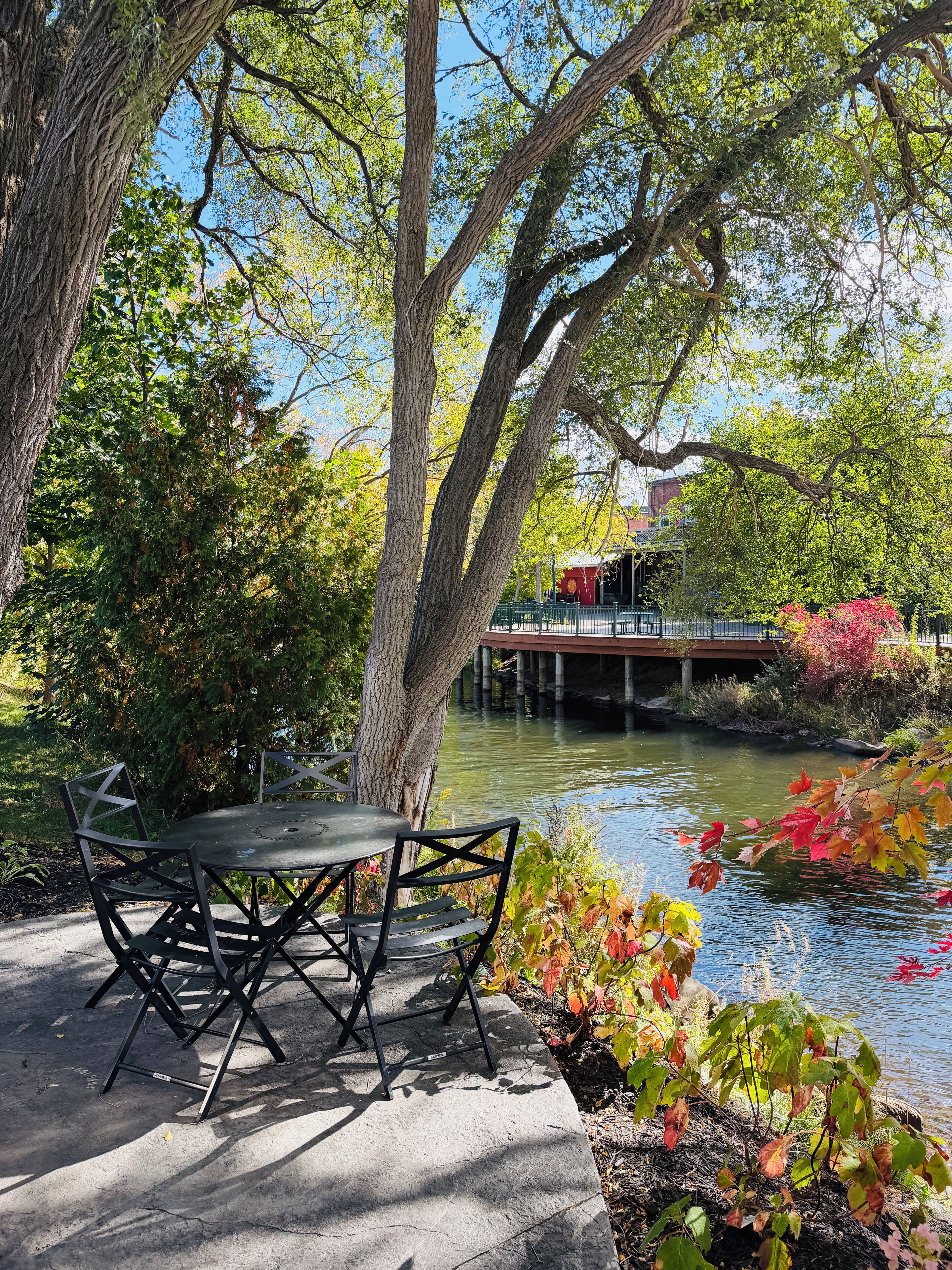 An outdoor seating area with a table and chairs, a concrete floor, and a view of a river with a bridge in the background.