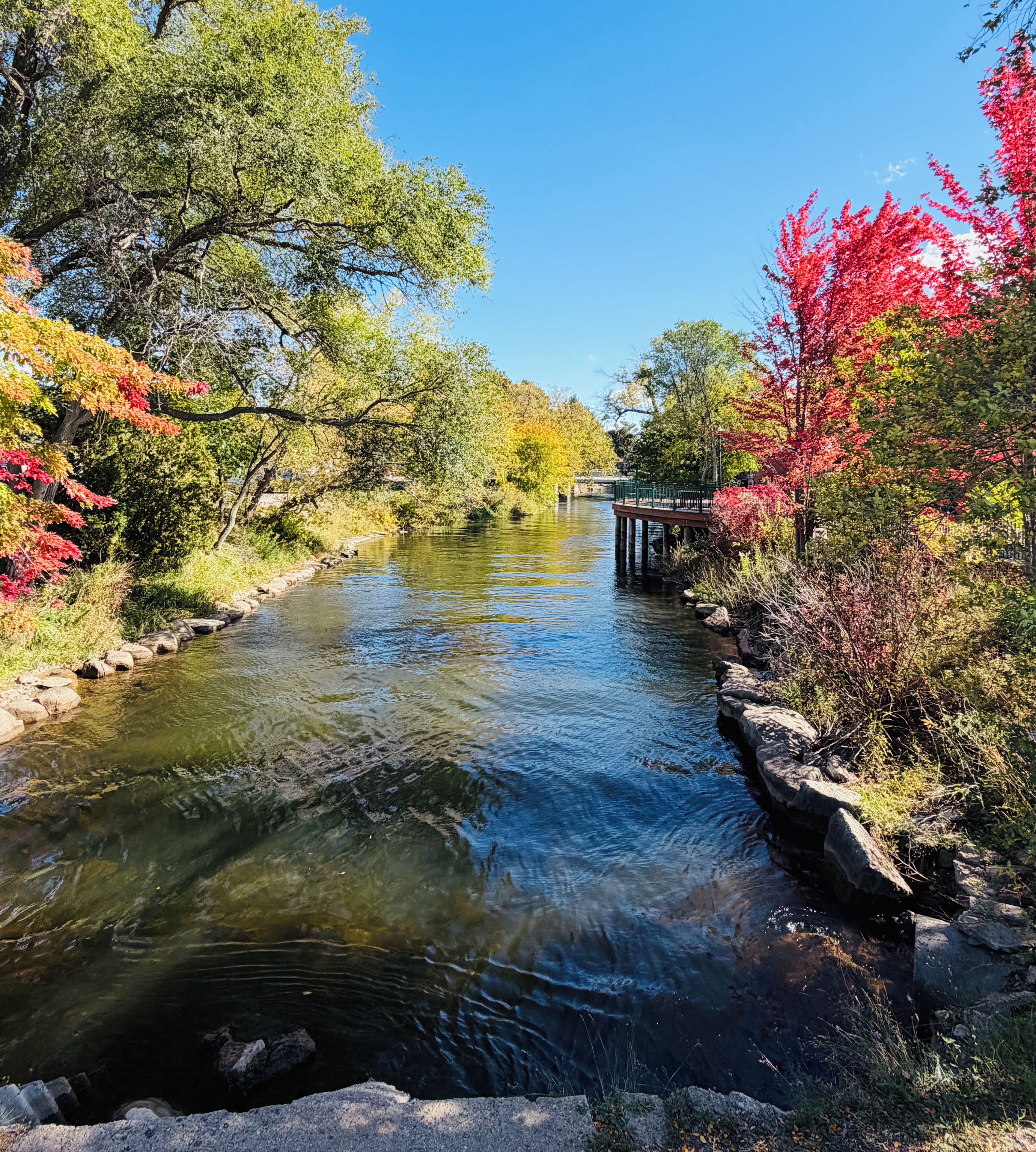A river with a stone bridge, surrounded by trees with autumn foliage.