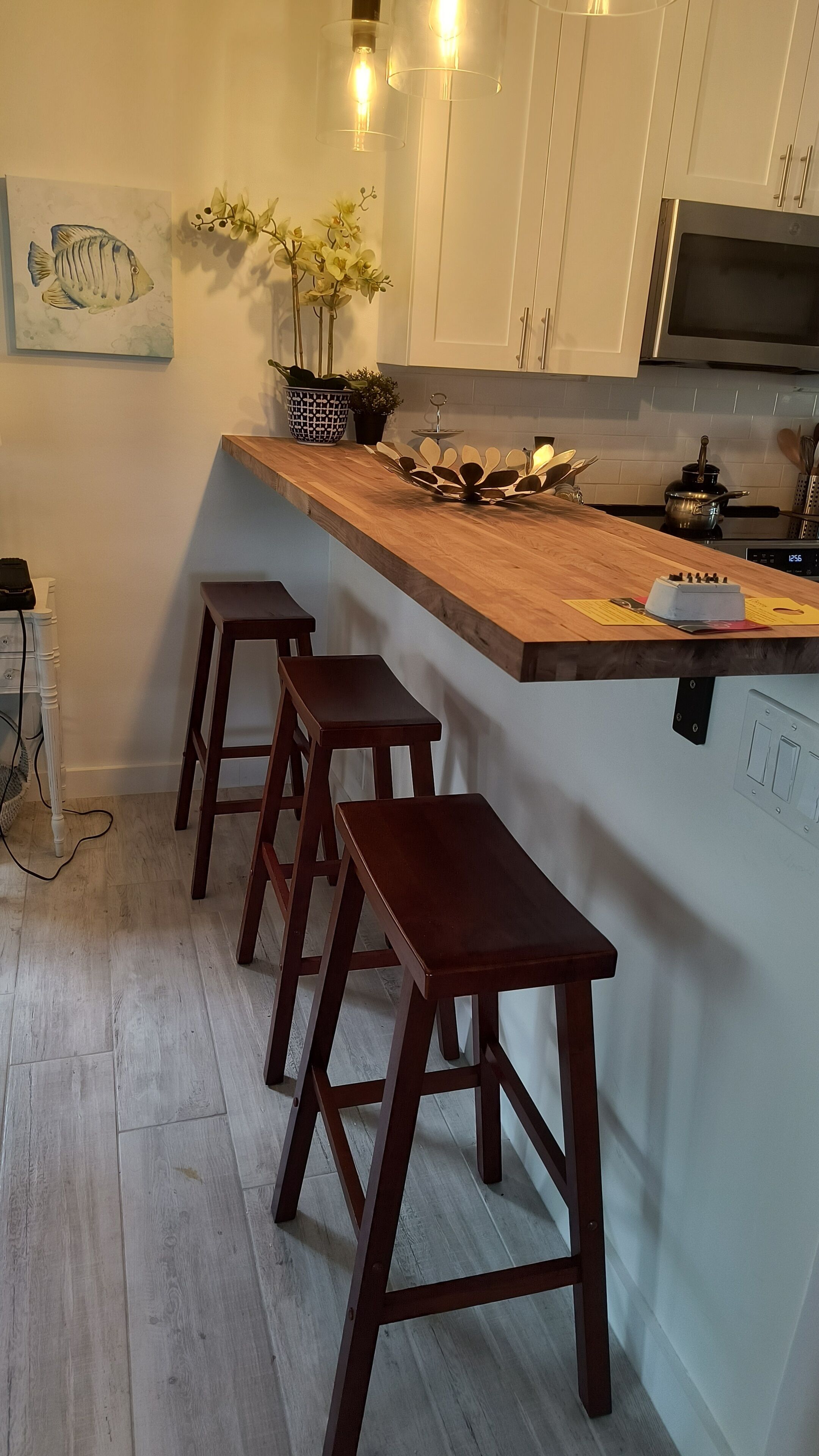 A kitchen with white cabinets, a wooden countertop, and three wooden stools.