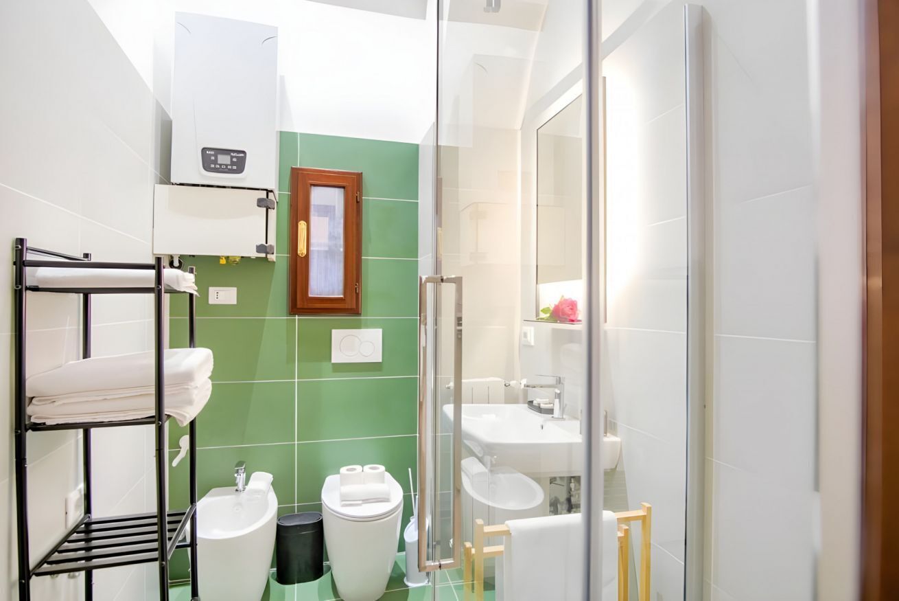 Un bany amb una paret verda, un lavabo blanc, un vàter, una dutxa i un assecagüdes.
