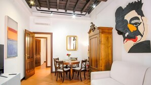 A living room with a white sofa, a dining table with chairs, a wooden cabinet, and a large abstract painting on the wall. - Elegantis.it Eat Pray and Love in Rome - Near Navona Square and Campo de' Fiori (Roma)
