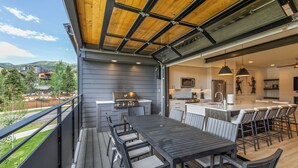 A modern kitchen with a central island, a dining area with a table and chairs, and a view of the surrounding landscape. - Aprés La Joy! AC, Amazing Indoor/Outdoor Kitchen & Deck Space, Private Hot Tub, Amenities! (Steamboat Springs)