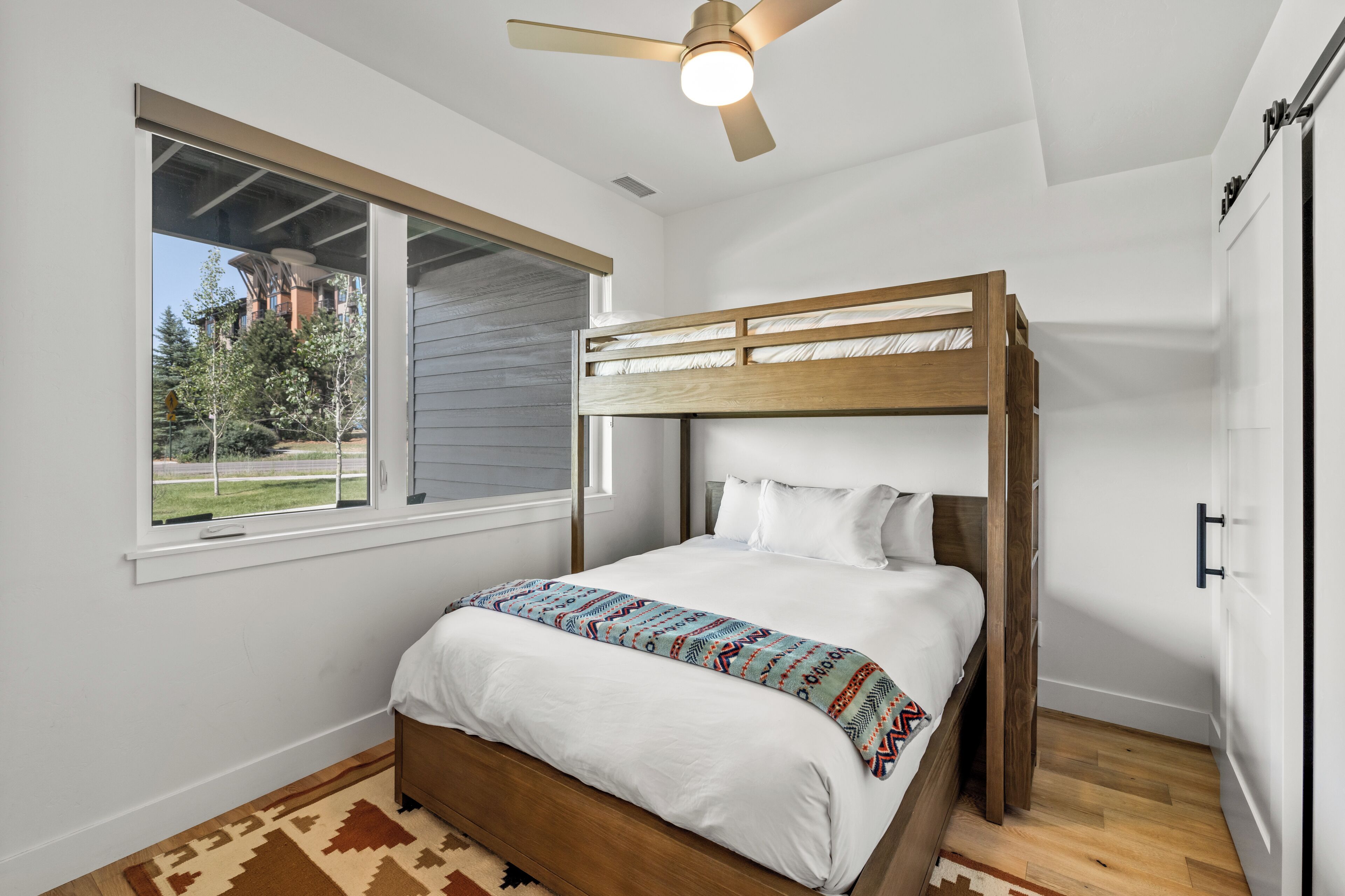 A bunk bed room with a window, ceiling fan, and a view of a building outside.