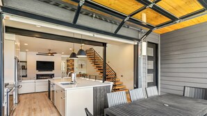 A modern kitchen with a central island, a dining area with a wooden table, and a staircase leading to an upper level. - Aprés La Joy! AC, Amazing Indoor/Outdoor Kitchen & Deck Space, Private Hot Tub, Amenities! (Steamboat Springs)