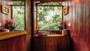 A wooden bathroom with a sink, two framed pictures, and a window with a view of trees. - Tominejo Ecolodge (Neira)