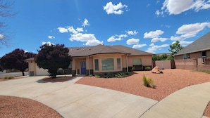 A single-story house with a beige exterior, a blue door, and a small front yard with red gravel and a single tree. - Your Kanab Retreat w/ Hot Tub, Game Room, Pet Friendly (Kanab)