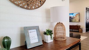 A wooden table with a framed welcome sign, a white vase with green plants, and a woven lamp. - Your Kanab Retreat w/ Hot Tub, Game Room, Pet Friendly (Kanab)