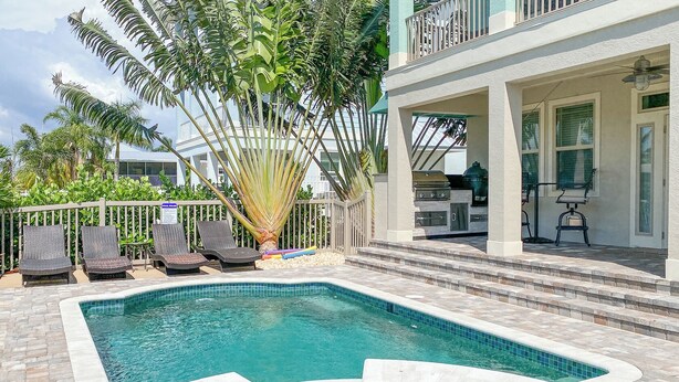 Une piscine entourée d’une terrasse en pierre, de chaises longues et d’un espace barbecue.