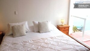 Un dormitorio con cama, almohadas, una mesita de noche y un ventanal con vistas.