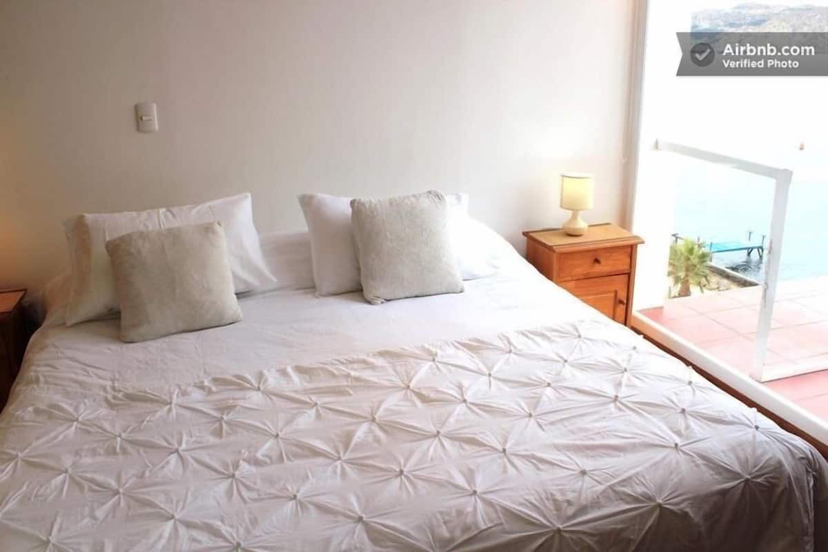 A bedroom with a bed, pillows, a nightstand, and a window with a view.
