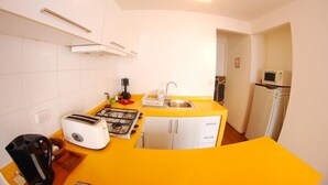 Una cocina compacta con encimera amarilla, armarios blancos, estufa a gas, tostadora y microondas.