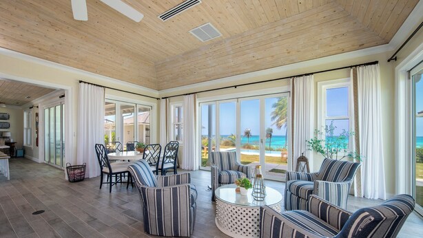 A spacious living area with a large window overlooking a beach, furnished with striped sofas and a round coffee table.