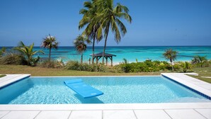 A swimming pool with a blue lounge chair, surrounded by palm trees and a view of the ocean.