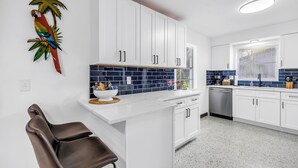 A modern kitchen with white cabinets, a blue backsplash, and a parrot decoration. - Oasis 3beds- 5minutes to beach -air hockey, foosball, pacman - beautiful murals! (Largo)