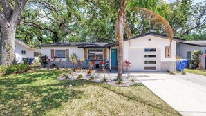 A single-story house with a front porch, a garage, and a small garden with various plants and a palm tree. - Oasis 3beds- 5minutes to beach -air hockey, foosball, pacman - beautiful murals! (Largo)