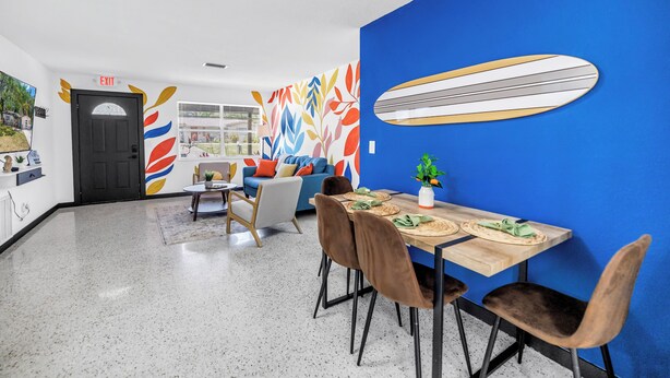 A dining area with a blue accent wall, a surfboard decoration, and a table set for two. - Oasis 3beds- 5minutes to beach -air hockey, foosball, pacman - beautiful murals! (Largo)