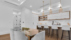 A modern kitchen with white cabinetry, a glass dining table, and bar stools.