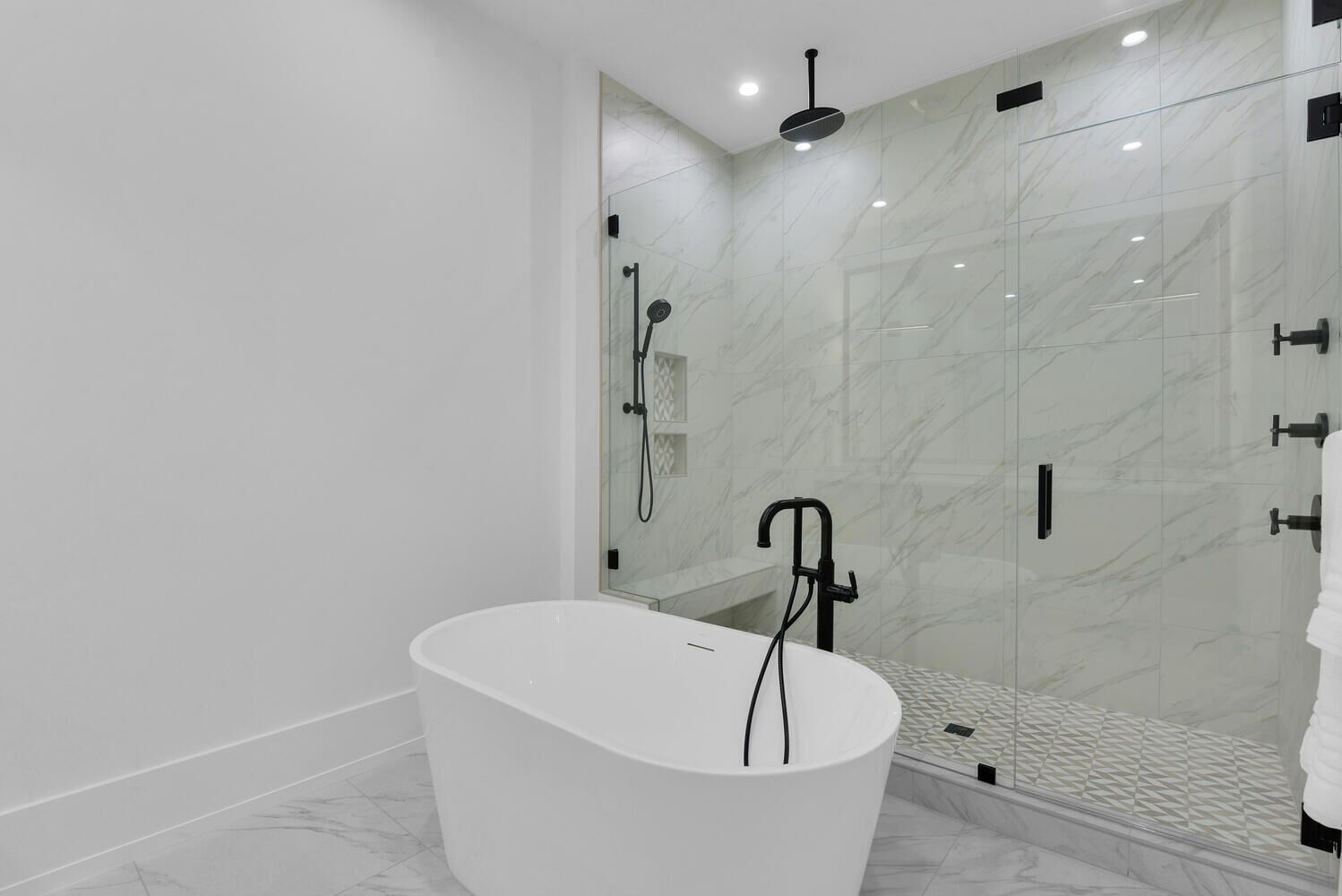 A modern bathroom with a freestanding bathtub, a glass shower enclosure, and marble walls.