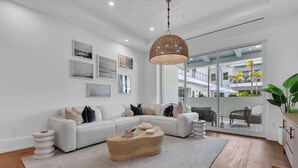 A modern living room with a white sofa, a wooden coffee table, and a large window overlooking a balcony with outdoor furniture.